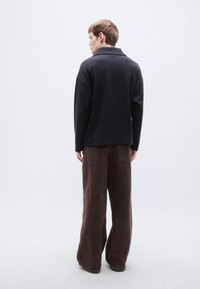 Pull noir à col avec une coupe décontractée, associé à un pantalon ample marron à jambes larges avec poches arrière.