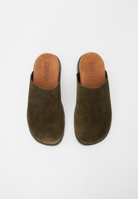 Zoccoli in suede verde scuro con punta arrotondata e apertura sul retro. Presentano una soletta in pelle color tan con il marchio "CAMPER." Design della suola liscia.