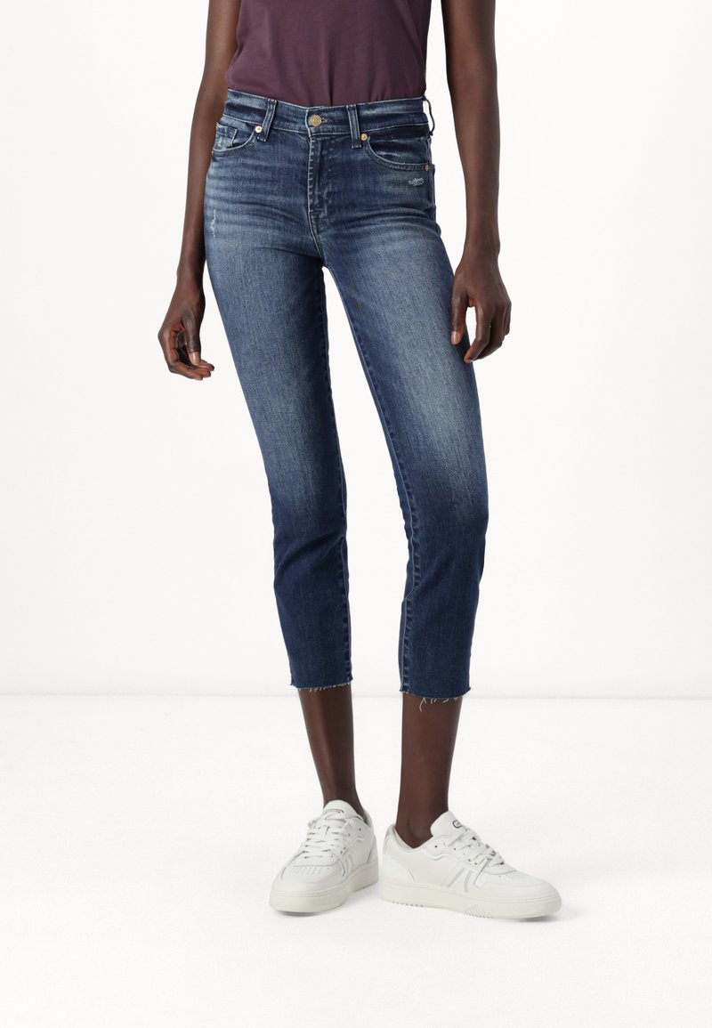 Sötétkék farmer cropped nadrág, elhalványult textúrával, slim fit, öt zsebbel és felkopott szegéllyel, fehér tornacipővel párosítva.