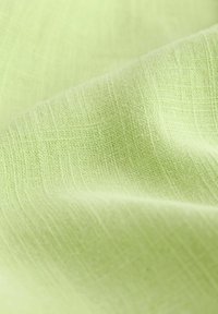 Svetlozelená tkanina s jemným, textúrovaným prepletom, ktorá má mäkký, prírodný vzhľad a jemný lesk. Hladký povrch s miernymi variáciami.