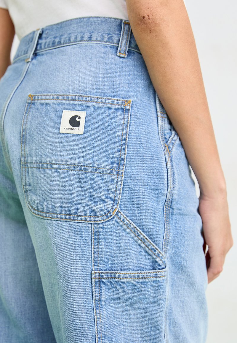 Lichtblauwe denim overall met een vierkante achterzak met het Carhartt-logo, contrasterende stiksels en een losse pasvorm.