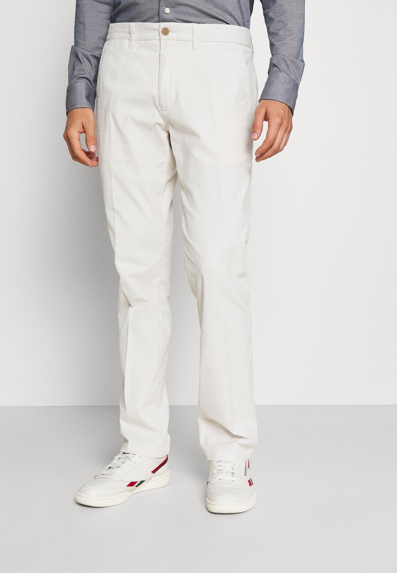 Pantalones de algodón blancos con corte recto, con cierre de botón y bolsillos. Combinados con zapatillas blancas con acentos en rojo y negro.