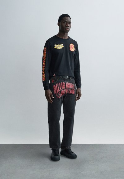 Μαύρο πουκάμισο με μακριά μανίκια και πολύχρωμα γραφικά μπροστά και στα μανίκια· συνδυασμένο με σκούρο τζιν με το κόκκινο λογότυπο "Billionaire Boys Club".