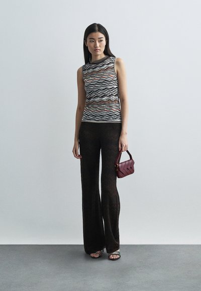 Top a maglia senza maniche con motivo ondulato in nero, marrone e crema; abbinato a pantaloni svasati scuri e strutturati; tiene una piccola borsa bordeaux.