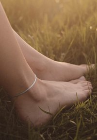 Silver chain anklet on bare foot with a natural, smooth texture, set against green grass in soft lighting.