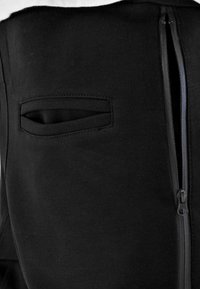 Black fabric garment featuring a side zip closure and a discreet pocket with a horizontal opening. Smooth texture, fitted design.