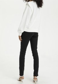 White sweatshirt with ribbed cuffs and hem, paired with black slim-fit jeans. Person wears white heels, facing away from the camera.