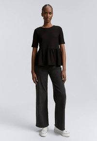 Haut péplum noir côtelé à manches courtes, associé à un jean large foncé et des baskets blanches. Texture lisse, design simple.