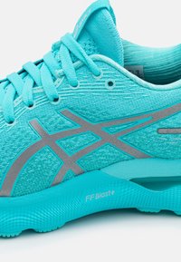 Gros plan d'une chaussure de course turquoise avec des lacets bleu clair, un logo de marque argenté et le texte "FF Blast+" sur la semelle rembourrée.