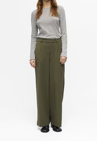 Šedý dlouhá rukáv ribovaný top v kombinaci s olivově zelenými širokými kalhotami a černými nazouvacími botami, zdůrazňující hladké textury a neutrální tóny.