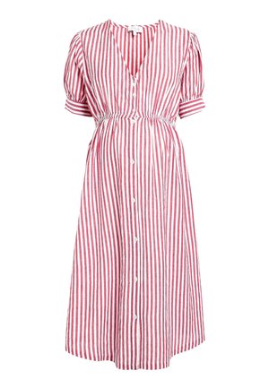 Kobieta w ciąży ubrana w czerwoną i białą, pionowo prążkowaną, zapinaną na guziki sukienkę, opierająca się o ścianę z jedną ręką na brzuchu.