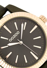 Montre au cadran noir avec des accents dorés, dotée d'une lunette texturée, de marqueurs d'heure argentés et d'un design minimaliste. Bracelet noir avec une texture lisse.
