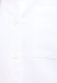 Biała lniana koszula z zapięciem na guziki, miękką fakturą i jedną kieszenią na piersi. Okrągły kołnierz oraz standardowe zapięcia na guziki.