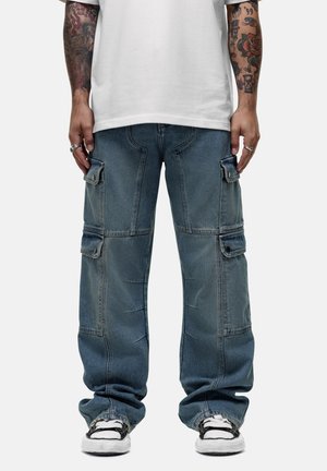 Baggy, blauwe denim cargobroek met meerdere zijzakken, contrasterende stiksels en een relaxte pasvorm. Gemaakt in combinatie met een wit t-shirt en sneakers.