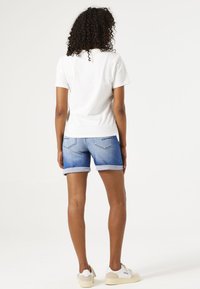 Camiseta blanca de manga corta combinada con pantalones cortos de mezclilla azules, doblados en el dobladillo. Zapatillas blancas con acentos claros. Textura suave, diseño casual.