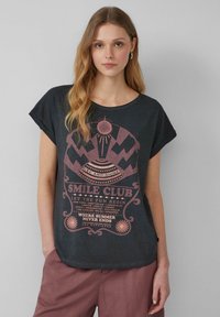 Donkergrijze katoenen t-shirt met korte mouwen, voorzien van een lichtroze grafisch ontwerp met tekst en patronen. Ontspannen pasvorm, casual stijl.