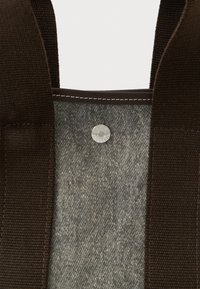 Barna pamut vászontáska szürke farmer belsővel. Ezüst patentgombos záródás és kontrasztos varrások találhatók a szélein.