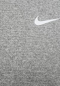Tejido atlético gris con un patrón texturizado, que presenta el logo de la paloma de Nike en blanco. El material parece suave y elástico.