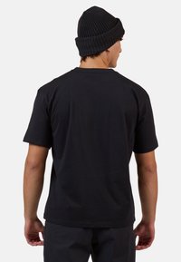 Černé bavlněné tričko s krátkým rukávem, kulatým výstřihem a volným střihem. Nosí se s černou pletenou čepicí; jednoduchý zadní pohled.