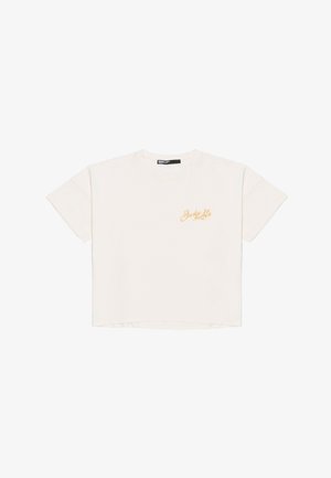 T-shirt court à manches courtes crème en coton doux, avec un logo brodé doré sur la poitrine gauche et une coupe décontractée.