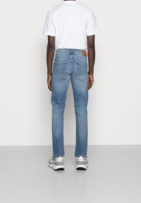 Vaqueros de denim azul de corte slim, con una cintura de altura media, que cuentan con una etiqueta de cuero marrón en la parte trasera y bolsillos traseros con costura curvada.