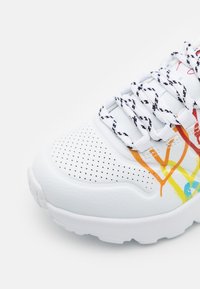 Białe sneakersy z kolorowymi, abstrakcyjnymi wzorami i perforowanymi detalami. Posiadają czarno-białe sznurówki w wzory oraz grubą, teksturowaną podeszwę.