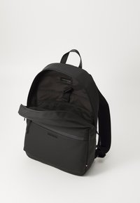 Zaino nero con un esterno in tessuto liscia, scomparto principale con zip, tasca frontale e spallacci imbottiti. Presenta il logo sul frontale.