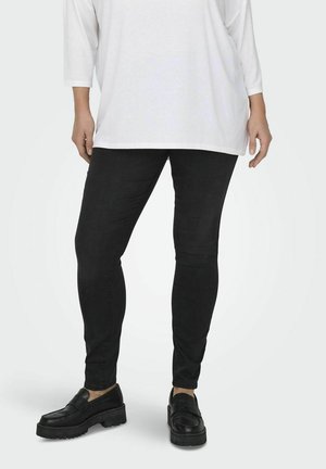 Jeans ajustados negros de denim con una textura suave, combinados con mocasines negros de plataforma con suela gruesa. Camiseta blanca de gran tamaño.
