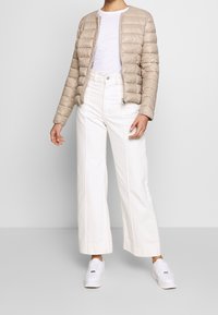 Giacca puffer beige con cuciture orizzontali, T-shirt bianca, jeans bianchi a vita alta e gamba larga, e sneakers bianche. Design semplice, linee pulite.