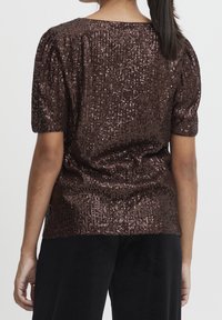 Bronsfärgad paljettblus med rundad halsringning och korta puffärmar. Strukturerad, reflekterar ljus, löst sittande och lätt rundad nederkant.