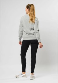 Grijze sweatshirt met een ontspannen pasvorm en geribbelde manchetten, gecombineerd met zwarte leggings en witte sneakers met grijze accenten.
