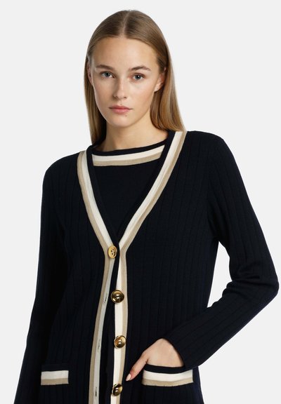 Marinblå ribbat cardigan med krämfärgade detaljer, guldknappar och fickor. Långa ärmar och V-halsdesign med kontrasterande horisontella linjer.