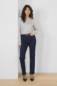 Maglione grigio a coste a maniche lunghe, jeans blu a gamba dritta con cuciture visibili, e tacchi neri a punta con dettagli a fascia.