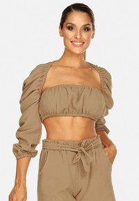 Beżowy krótki top z bufkami, teksturowany materiał, elastyczny pasek na dole, zestawiony z dopasowanymi spodniami o wysokim stanie i przewiązanym paskiem.