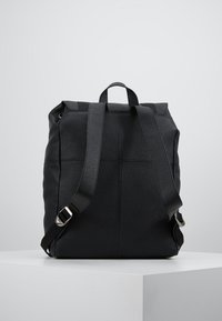 Svart läderryggsäck med strukturerad yta, justerbara remmar och handtag på toppen. Har silverfärgade detaljer och minimalistisk design.