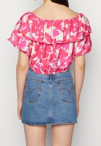 Blouse à épaules dénudées avec un motif floral rose et des volants, associée à une mini-jupe en jean bleu clair avec poches arrière et détails de couture.