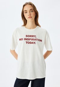 Hvid bomulds T-shirt med korte ærmer og rund halsudskæring, med fed burgunder tekst: "SORRY, NO INSPIRATION TODAY."