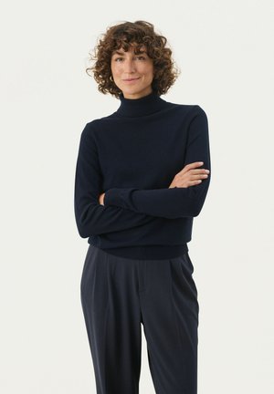 Marinblå polotröja med en figurnära design, tillverkad av mjukt tyg; kombinerad med lösa mörka byxor med ribbade cuffs och midja.