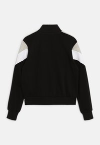 Chaqueta negra con cremallera y cuello alto, con hombros en bloque de color gris y blanco. Está hecha de un tejido suave y elástico con puños acanalados.