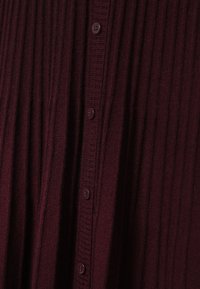 Burgundijas ribots kardigāns ar sešiem pogām, teksturēta auduma un piegulošs fit, ar vertikālu svītru rakstu priekšā.