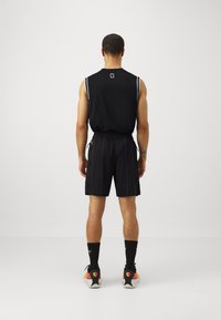 Top fitness senza maniche nero con strisce bianche, abbinato a pantaloni corti neri con cordino e un motivo sottile, calze nere e sneakers colorate.