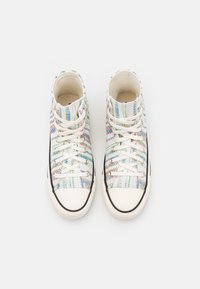 Zapatillas altas con un patrón trenzado multicolor, tejido blanco, suela de goma negra y cierre de cordones clásico.