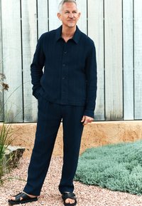 Marineblå tekstureret skjorte med spidst krave, knaplukning og matchende bukser. Bruges med sorte slidesandaler. Naturlig baggrund.