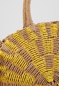 Sac en paille tressée présentant des fibres de la couleur naturelle beige et d'un jaune vif, avec une forme ronde et deux poignées robustes pour le transport.