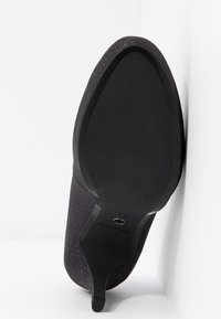 Chaussure à talon haut noire à bout pointu avec un talon fin, vue du côté de la semelle sur fond blanc.