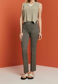 Beige geribbelde mouwloze top gecombineerd met strakke geruite broek in grijs, zwart en wit; model draagt zwart-witte sandalen.