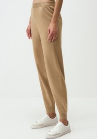 Joggeurs en tricot beige avec une taille côtelée et des chevilles resserrées, associés à des baskets blanches. Texture lisse et design ample pour le confort.