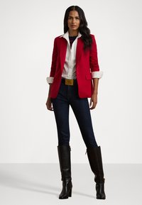 Red blazer with rolled cuffs, white collared shirt, dark jeans, and knee-high black leather boots. Gold belt accentuates the waist.