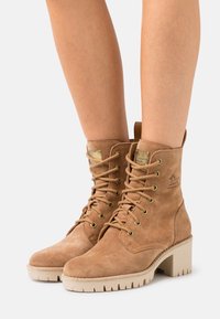 Bottines en suède tan à lacets avec un talon sérré, dotées d'œillets en métal, d'un logo embossé et d'une semelle en caoutchouc texturé.