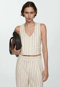 Korte crèmekleurige tanktop met verticale zwarte strepen, V-halslijn, knoopsluiting aan de voorkant, gecombineerd met bijpassende gestreepte gepaste broek en een zwarte handtas.
